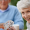 Two seniors playing bridge, in the foreground a woman looks at the camera and smiles, holding up her bridge hand. To illustrate and article titled Cognitive benefits of bridge and moderate strategic gaming