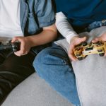 Closeup of two people holding joycons, sitting on couch together enjoying relaxed gaming