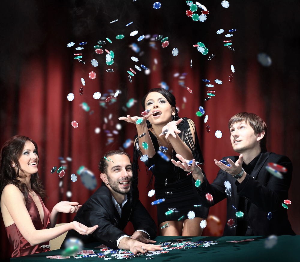 Image of four people enjoying a winning game of cards in a casino, casino chips thrown into the air. Best Casino Games for Real Money