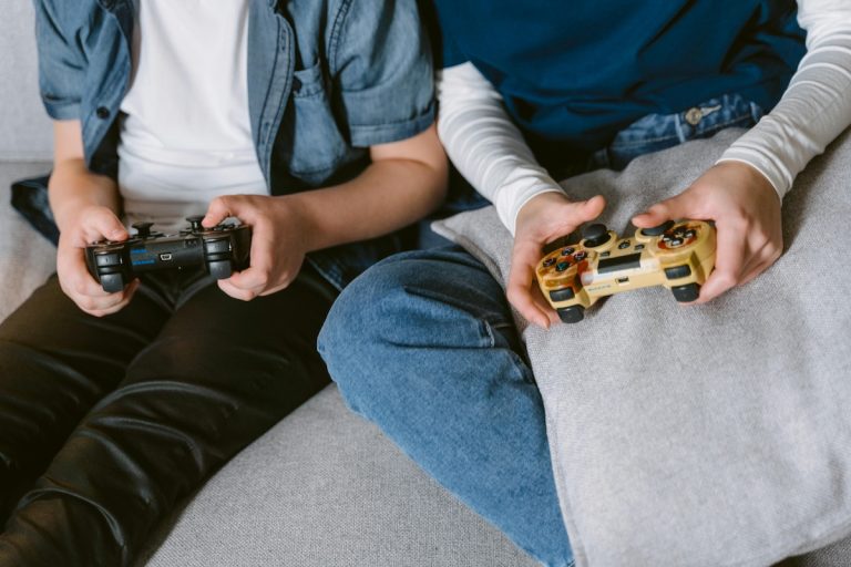 Closeup of two people holding joycons, sitting on couch together enjoying relaxed gaming