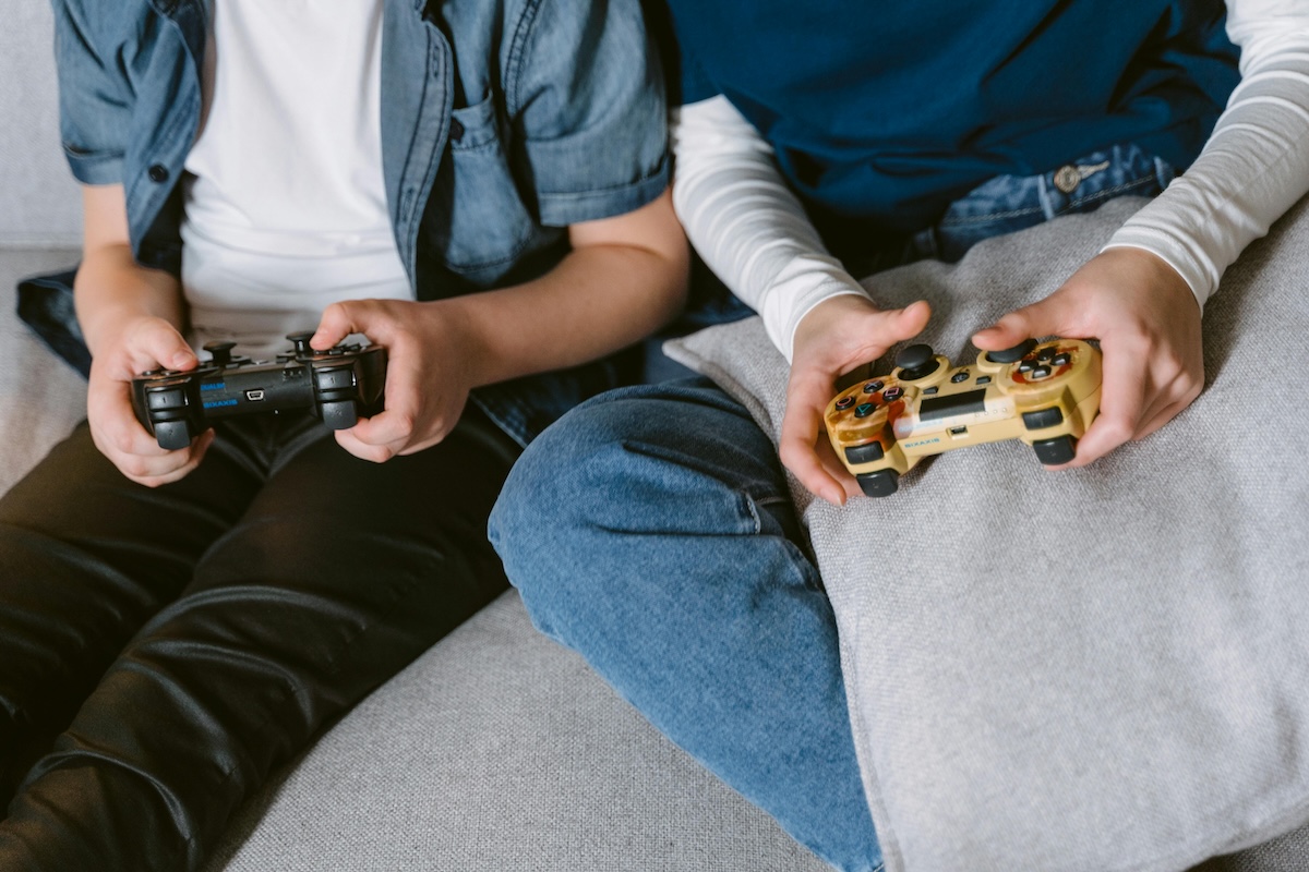 Closeup of two people holding joycons, sitting on couch together enjoying relaxed gaming